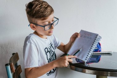 Gözlüklü Latin çocuk defterine resim çiziyor. Okula, çocukluğa. Ödev ve dersler.