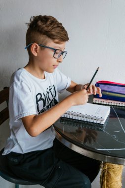 Gözlüklü Latin çocuk defterine resim çiziyor. Okula, çocukluğa. Ödev ve dersler.