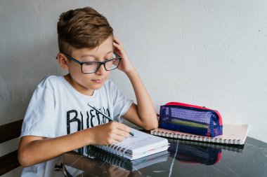 Gözlüklü Latin çocuk defterine resim çiziyor. Okula, çocukluğa. Ödev ve dersler.