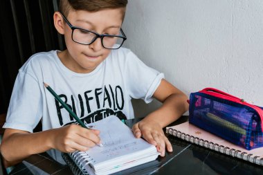 Gözlüklü Latin çocuk defterine resim çiziyor. Okula, çocukluğa. Ödev ve dersler.