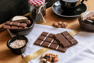 Çikolata parçalı kurabiyeler, siyah beyaz çikolatalar, küçük bir kase yulaf ezmesi ve fındık. Uluslararası Çikolata Günü.