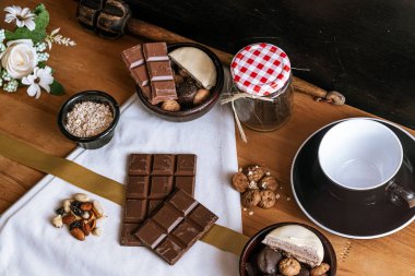 Çikolata parçalı kurabiyeler, siyah beyaz çikolatalar, küçük bir kase yulaf ezmesi ve fındık. Uluslararası Çikolata Günü.