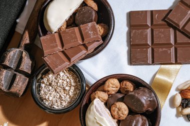 Çikolata parçalı kurabiyeler, siyah beyaz çikolatalar, küçük bir kase yulaf ezmesi ve fındık. Uluslararası Çikolata Günü.