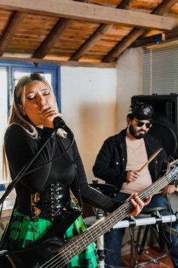 Bas gitar çalan kadın şarkıcı. Grubun provası evde. Uluslararası müzik günü.