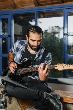 Sakallı bir adam elektro gitar çalıyor. Grubun provası evde. Uluslararası müzik günü.