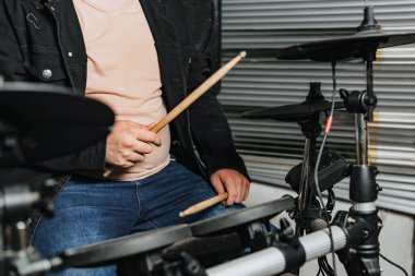 Elektrikli davul çalan gözlüklü ve şapkalı adam. Mikrofon, gitar, bas. Bando evde. Uluslararası müzik günü.