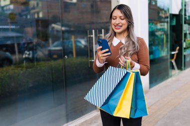 Kadın cep telefonuyla konuşuyor. Kara Cuma indirimleri sırasında fotokopi alanı ile birlikte. Mutlu müşteri, renkli çantalar..