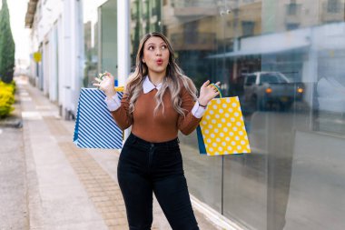 Alışveriş yapan mutlu kadın, siyah cuma günü sarı ve mavi çantalı ürünleriyle kameraya bakıyor. İnanılmaz indirimler..