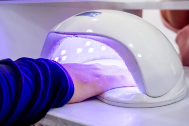 Yarı kalıcı tırnak cilası kururken, bir kadının elleri lambanın içinde. Çivi Spa 'sı. Güzellik ve moda.