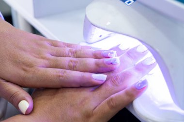 Yarı kalıcı tırnak cilası kururken, bir kadının elleri lambanın içinde. Çivi Spa 'sı. Güzellik ve moda.