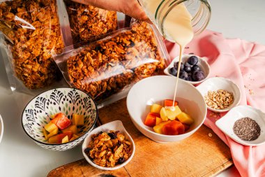 Ev yapımı granola, meyveli mango, papaya ve üzümlü sağlıklı kahvaltı yoğurdu servis eden el.