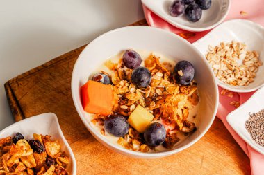 Ev yapımı granola ve meyvelerle karıştırılmış yoğurtlu sağlıklı kahvaltı: mango, papaya ve üzüm..