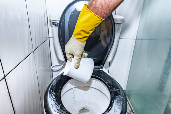 Adult Colombian Latino male washing and rinsing the toilet in his home bathroom.