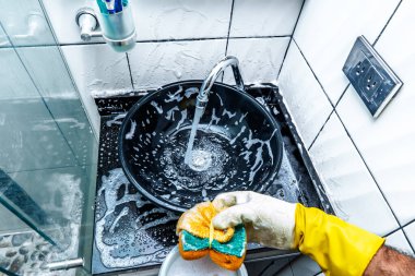 Yetişkin Kolombiyalı erkek sabunlanıyor, banyo lavabosunu temizliyor ve süngerle yıkıyor. Ev işi yapan insan kavramı.