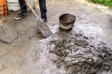 İnşaat için çimento karıştıran insan bacakları ev yenileme projesinde yanında kürek ve kova ile birlikte.