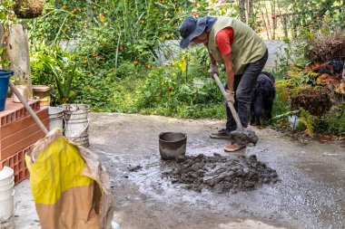 Yaşlı Kolombiyalı adam evindeki yenileme projesinde çimento ve inşaat suyunu kürekle karıştırıyor..