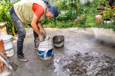 Yaşlı Kolombiyalı bir adam ev yenileme projesinde inşaat suyuyla çimento karıştırıyor.