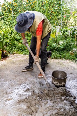 Ev yenileme projesine çimento ve inşaat suyu karıştıran yaşlı Kolombiyalı bir adam.