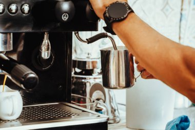 Kolombiyalı baristanın ellerinin Kolombiyalı kahve dükkanında kapuçino kahvesi hazırlamak için sütü kapuçino makinesinde dokuduğu fotoğrafı.