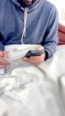 Yatağında gözlüklü, sakallı Kolombiyalı mestizo yetişkin bir adamın kredi kartıyla internetten bir şeyler alabildiğini gösteren bir video..