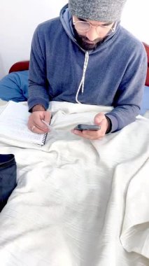 Yatağında gözlüklü, sakallı Kolombiyalı mestizo yetişkin bir adamın kredi kartıyla internetten bir şeyler alabildiğini gösteren bir video..