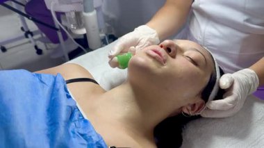 Koyu renk saçlı, Kolombiyalı yetişkin bir kadının kaplıcada yağlı ve soğuk aletlerle yüz masajı yaptırdığı bir video.. 