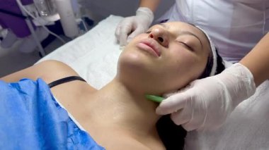 Koyu renk saçlı, Kolombiyalı yetişkin bir kadının kaplıcada yağlı ve soğuk aletlerle yüz masajı yaptırdığı bir video.. 