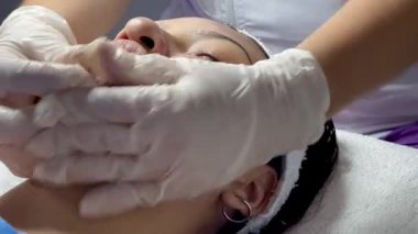 Koyu renk saçlı, Kolombiyalı yetişkin bir kadının kaplıcada yağlı ve soğuk aletlerle yüz masajı yaptırdığı bir video.. 