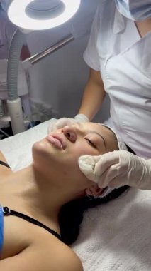 Koyu renk saçlı, Kolombiyalı yetişkin bir kadının kaplıcadaki yüz masajı videosu. Yağ ve soğuk malzemelerle masaj yaptırıyor ve derisi soyulmuş.. 