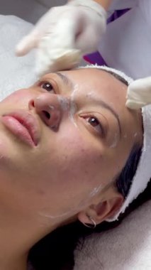 Koyu renk saçlı, Kolombiyalı yetişkin bir kadının kaplıcadaki yüz masajı videosu. Yağ ve soğuk malzemelerle masaj yaptırıyor ve derisi soyulmuş.. 