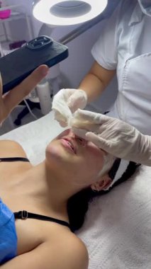 Koyu saçlı, genç, Kolombiyalı melez bir kadının elinde cep telefonuyla spa 'da çekilmiş videosu. Kil maske cildinin sağlığını iyileştirmek için kullanılıyor.. 