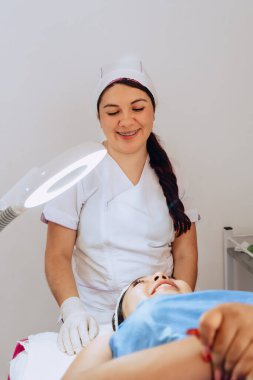 Güzellik merkezindeki iki genç Kolombiyalı kadının fotoğrafı. Dermatolog müşterisine yüz temizleme ameliyatında ne yapacağını anlatıyor..