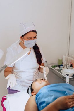 Güzellik merkezindeki bir güzellik uzmanının genç, melez bir Kolombiyalı kadına yüz temizleme tedavisinin bir kısmını açıklarken fotoğrafı..