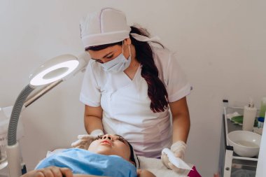 Güzellik merkezindeki bir güzellik uzmanının, yüz temizleme tedavisini tamamlamak için genç melez bir Kolombiyalı kadının yüzüne güneş kremi sürerken fotoğrafı..