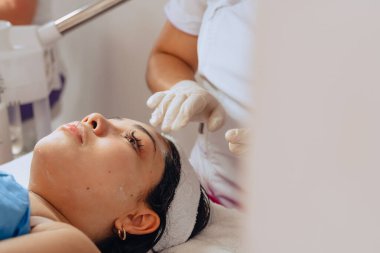 Güzellik merkezindeki genç mestiza Kolombiyalı kadının fotokopi aralıklı fotoğrafı cilt temizleme tedavisini tamamlamak için yüzüne güneş kremi sürerken cilt doktorunun ellerini gösteriyor..
