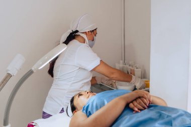 Bir cildiyecinin, müşterisinin yüz temizleme ameliyatında kullanacağı ürünleri kontrol edip hazırlarken çekilmiş bir fotoğrafı. Güzellik merkezinde iki genç Kolombiyalı mestiza..