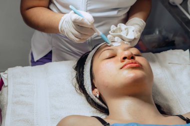 Yüzüne çamur maskesi takan estetisyen Kolombiyalı genç bir kadının yüz temizleme kliniğinde fotoğrafı..