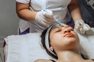 Yüzüne çamur maskesi takan estetisyen Kolombiyalı genç bir kadının yüz temizleme kliniğinde fotoğrafı..