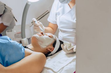Cildiyecinin yüz temizleme kliniğindeki genç Kolombiyalı Latin kadının yüzüne çamur maskesi sürerken çekilmiş bir fotoğrafı..