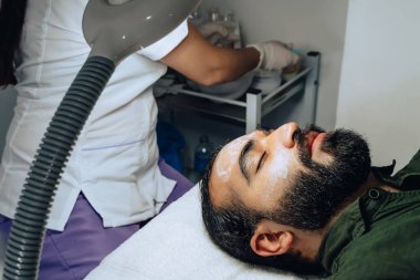 Kolombiyalı mestizo sakallı yetişkin bir erkek için profesyonel deri yüzme, nemlendirici ve yüz temizleme fotoğrafı..