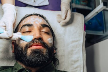 Sakallı yetişkin bir Kolombiyalı mestizo adam için profesyonel deri yüzme, nemlendirici ve yüz temizleme tedavisinin uzay fotokopisi..