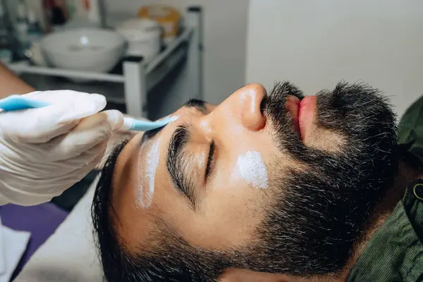 Sakallı, yetişkin bir Kolombiyalı mestizo adam için profesyonel deri yüzme, nemlendirici ve yüz temizleme tedavisinin yakın plan fotoğrafı..