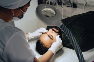 Cildiyecinin, sakallı Kolombiyalı mestizo yetişkin bir erkeğin yüzündeki nemlendirici jeli temizlerken çekilmiş resmi. Profesyonel bir cilt soyma, nemlendirici ve yüz temizleme tedavisi sırasında..