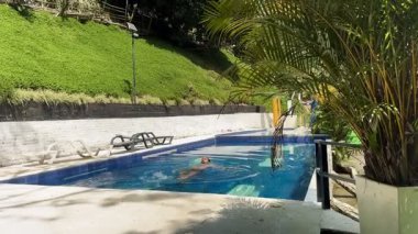 Kolombiyalı uzun saçlı ve sakallı bir adam güneşli bir tatil gününde bir otel havuzunda sırtüstü yüzüyor.