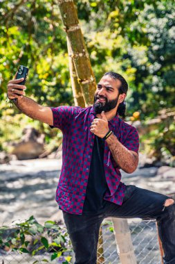 Orta kahverengi tenli Kolombiyalı bir adam kameraya yakın selfie çekerken Santuario, Risaralda, Kolombiya 'daki kırsal oteldeki tropik bitki örtüsü arasında çenesine dokunuyor.