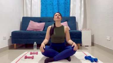 Nilüfer çiçeğiyle meditasyon yapan bir kadının geniş açı çekimi vinç tarzı kamera eğiminin ev egzersiz sahnesini ortaya çıkardığını gösteriyor.