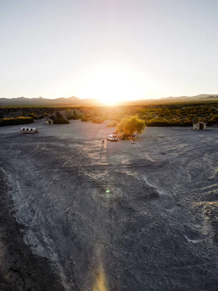 Aerial view drone shot of van life living and working in remote area of nevada usa desert with sun setting in distance with warm orange hues and bright over exposed sky for copy space.