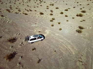 Güney Nevada 'da, karavan yaşam platformuna monte edilmiş güneş panelleri ve bisikletlerle kuru bir göl yatağında giden kendi kendine dönüştürülmüş bir karavan aracının hava görüntüsü..
