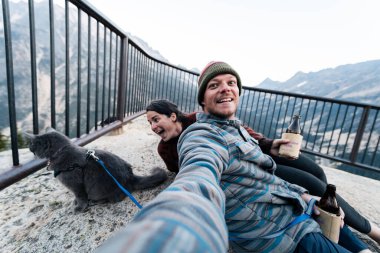 30 'lu yaşlarda beyaz bir kadın kocası ve kedisiyle oturup içkisini yudumlarken gri mavi Rus kedisini Washington' da popüler bir dinlenme yerinde vahşi doğa ormanında tasma takıyor..