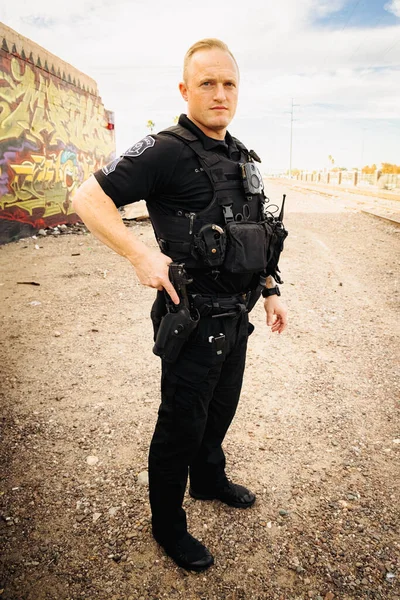 Vertical image of white male caucasian police officer reaching down and places hand on his weapon hand gun and pulls gun out of holster on hip. Full body shot.